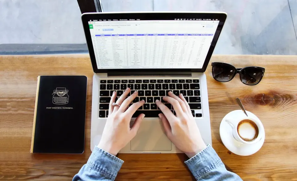 A person typing on a laptop next to a cup of coffee