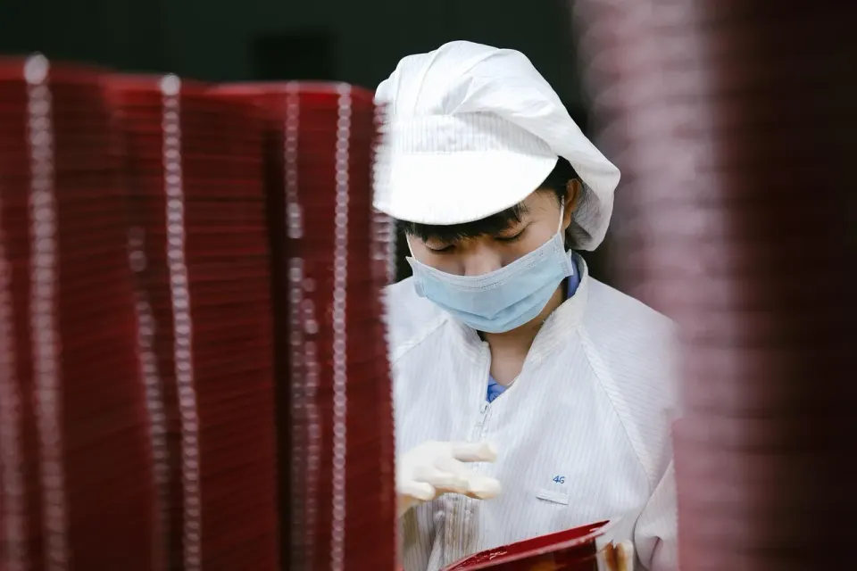 A factory worker in a cleanroom suit and mask checking parts